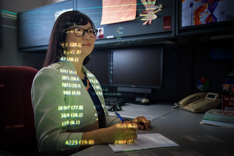 Mary Schroeder works at a computer with light of numbers projecting on her