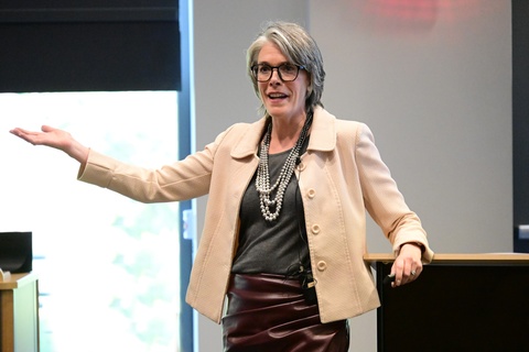 Susan Winckler speaking and gesturing with one hand. She is leaning against a podium.