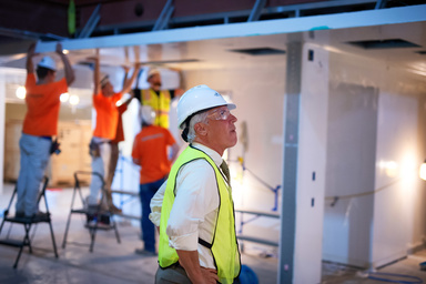 Dennis Erb in construction gear looking at new space with construction workers behind him