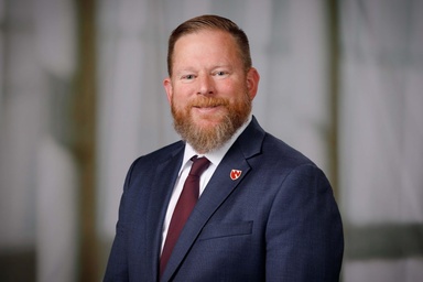 Headshot of a red-haired man in a blue suit jacket with a red tie. 