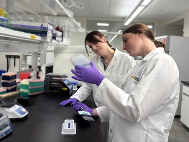 Faculty Marie Gaine and graduate student Emma Simpson in white coats in a pharmacy lab 