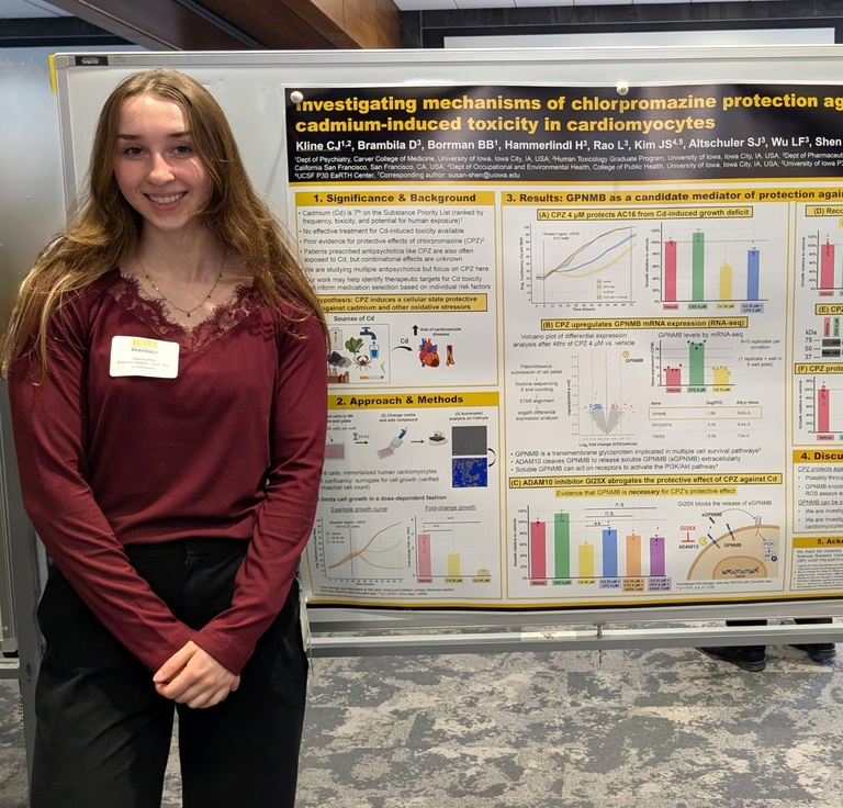 Student stands beside a research poster on drug protection against cadmium-induced toxicity, smiling in a conference setting. The poster features charts, graphs, and study findings displayed on a presentation board.