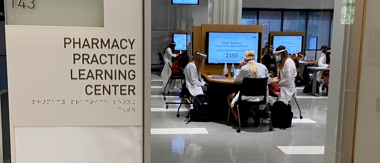 sign of the Pharmacy Practice Learning Center (PPLC), with students working at tables in the background