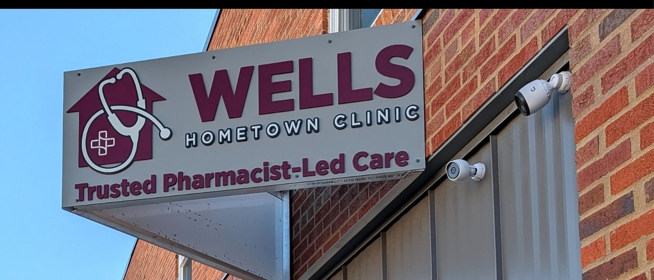 Sign reading Wells Hometown Clinic with stethoscope logo mounted on brick building.